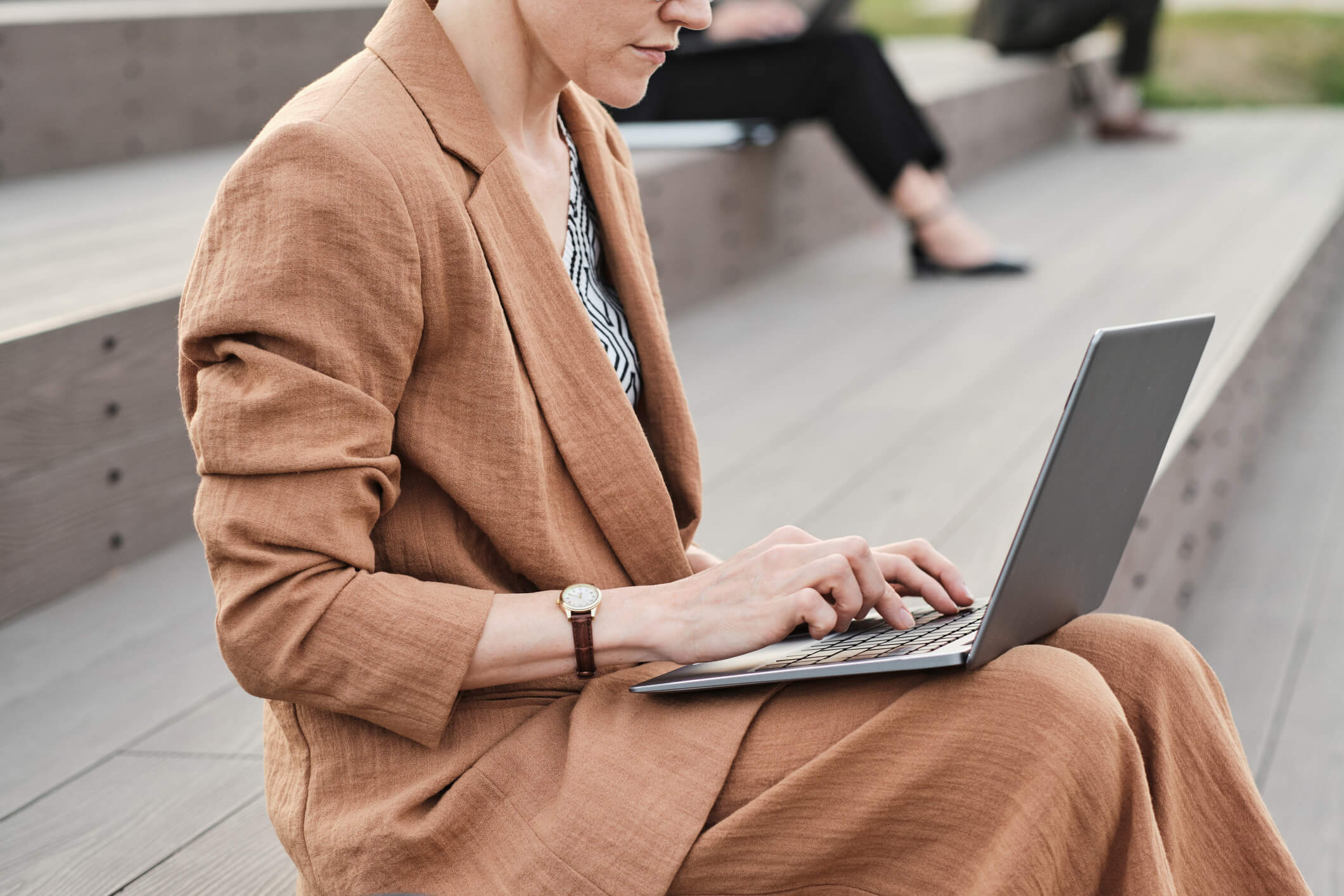 A close up of a woman sitting outside and using a laptop; she has a serious expression.